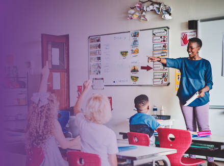 Teacher calling on students with their hands raised; view is the at the side of the classroom